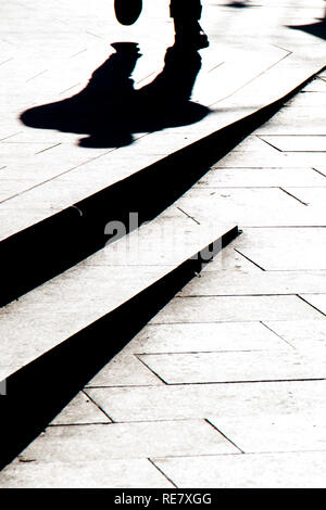 Silhouette floue ombre d'un homme marchant sur un trottoir de la ville avec des marches en noir et blanc de contraste élevé Banque D'Images