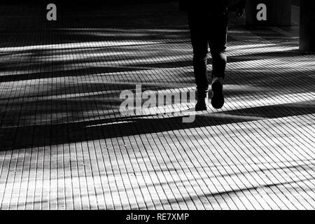 Ombre d'une silhouette floue les jambes d'une personne qui marche sur une passerelle d'arcade de la ville en noir et blanc de contraste élevé Banque D'Images