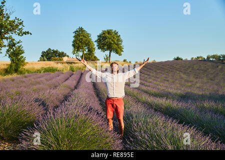 Le beau jeune homme brutal avec de longs cheveux de brunette pose dans le champ de lavande Banque D'Images