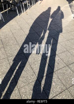 De longues ombres de deux personnes sur le trottoir. Soleil du soir lumineux. Banque D'Images