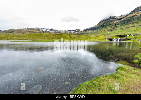 Grand angle, Islande Grundarfjordur vue paysage de cascade Kirkjufell monument avec de l'eau en vert clair transparent jour nuageux Banque D'Images