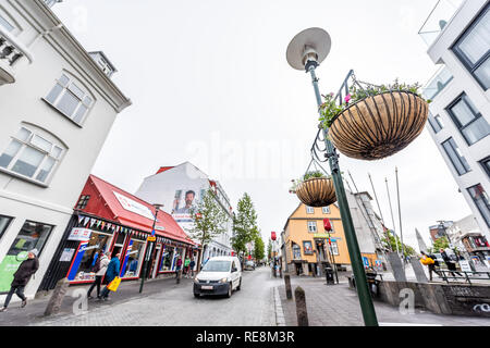 Reykjavik, Islande - 19 juin 2018 : les touristes les gens marcher sur rue avec voiture sur route et trottoir en centre-ville centre de paniers de fleurs suspendus, pour la lampe Banque D'Images