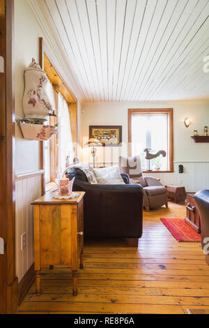 Cabinet en bois ancien, un canapé en cuir brun et tissu fauteuil capitonné dans la salle de séjour à l'intérieur d'une ancienne maison de style cottage Canadiana 1892 Banque D'Images