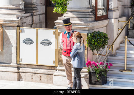 Londres, Royaume-Uni - 22 juin 2018 : Porter une tenue traditionnelle de portier et de vêtements chapeau avec veste rouge debout parlant à touriste par entrée de Manda Banque D'Images