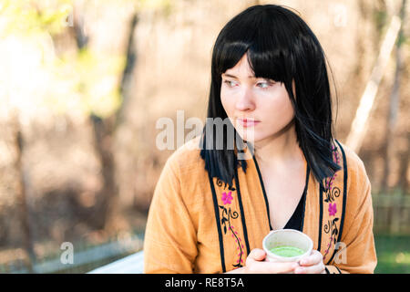 Woman holding tea cup sur l'extérieur dans le jardin avec fille et vert matcha cheveux noirs et des vêtements asiatiques Banque D'Images