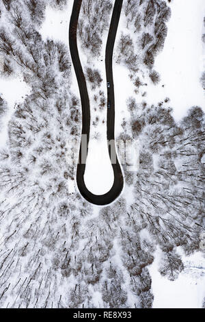 Vue aérienne d'une belle route serpentine avec quelques voitures qui passent par elle. Paysage spectaculaire composée d'une forêt de pins et de neige blanche. Banque D'Images