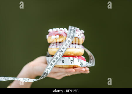 Trois des beignets sucrés recouvert de ruban de mesure sur la main sur le fond vert. La mauvaise alimentation et de l'adiposité concept Banque D'Images