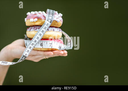 Trois des beignets sucrés recouvert de ruban de mesure sur la main sur le fond vert. La mauvaise alimentation et de l'adiposité concept Banque D'Images