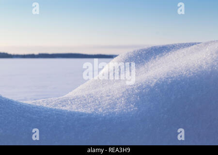 Close-up of fresh snow brillant sur un banc de neige sur une journée ensoleillée en hiver. Le lac gelé et enneigé flou en arrière-plan. Banque D'Images