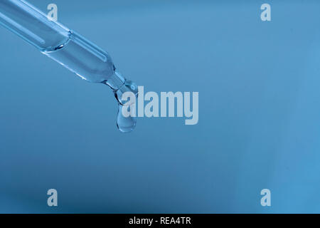Une goutte d'eau dans une pipette contre fond bleu Banque D'Images