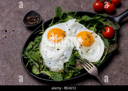 Deux œufs frits, Sunny Side Up, le pan avec des herbes, roquette, épinards, tomates cerise et poivre, avec une fourchette d'un fond brun. Concept de vie sain Banque D'Images