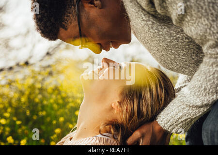 Close up of young man and woman looking at les uns les autres avec amour. L'Interracial couple outdoors en prairie. Banque D'Images