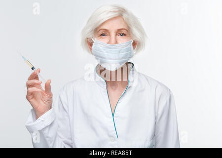 Femme médecin senior studio isolé sur mur blanc tenant la seringue d'injection d'anti-vieillissement Banque D'Images