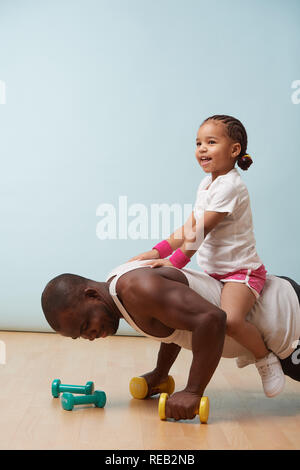 Beau black jeune père fait pousser ups sur haltères avec sa jolie petite fille lui. Ils possèdent tous deux des il grand temps. À l'intérieur. Banque D'Images