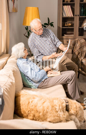 Portrait de l'adorable senior couple at home reading newspaper in sunlit salle de séjour Banque D'Images