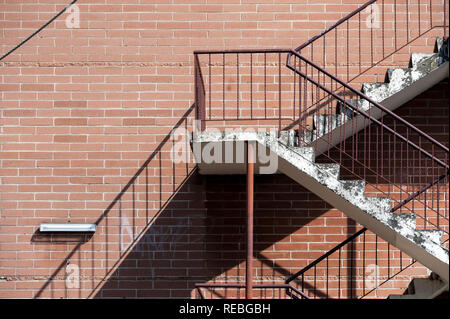 Escaliers en béton avec garde-corps métal rouge contre un mur de brique rouge de la création d'une diagonale forte d ombre Banque D'Images