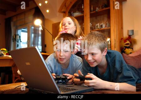 Frères et sœurs, 7, 11, 13 ans, avec un ordinateur portable dans le salon, jouant un jeu d'ordinateur de course de voiture Banque D'Images