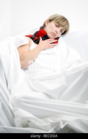 Une jeune femme avec un mal de gorge et un rhume au lit, avec un foulard Banque D'Images