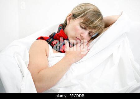 Une jeune femme avec un mal de gorge et un rhume au lit, avec un foulard Banque D'Images