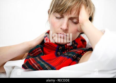 Une jeune femme avec un mal de gorge et un rhume au lit, avec un foulard Banque D'Images