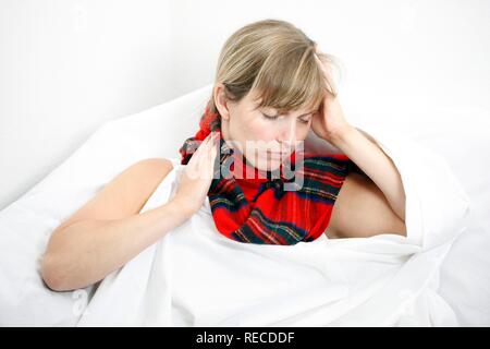 Une jeune femme avec un mal de gorge et un rhume au lit, avec un foulard Banque D'Images