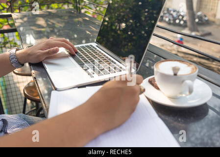 Jeune homme travaillant sur ordinateur portable et la rédaction de notes Banque D'Images