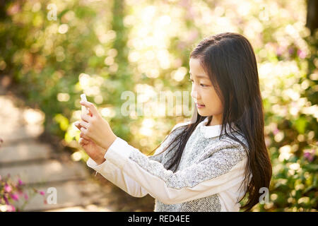 Belle petite fille asiatique aux cheveux longs en tenant une fleur fond contre selfies using cellphone Banque D'Images