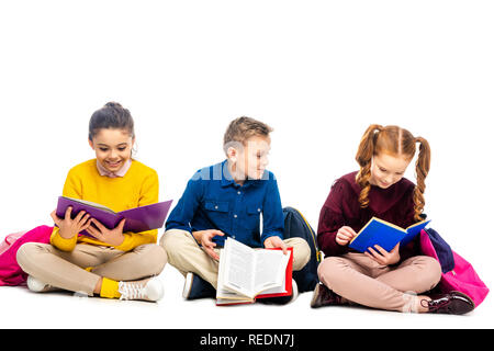 Cheerful écoliers assis et la lecture de livres isolated on white Banque D'Images