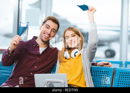 Joyeux petit ami et petite amie de nationalités avec les billets à l'aéroport Banque D'Images