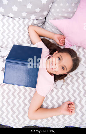 Lit enfant fille lay read book vue d'en haut. Kid se préparer à aller au lit. Temps agréable dans une chambre confortable. Kid fille cheveux longs pyjamas mignons vous détendre et lire livre. Encourager les habitudes utiles. Satisfait de professionnels. Banque D'Images