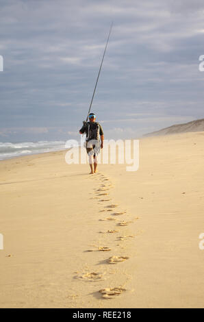 Surfez pêcheur avec sa canne à pêche à pied dans le sable sur une plage de l'océan Atlantique. Adventure pêche, pêche sauvage Banque D'Images