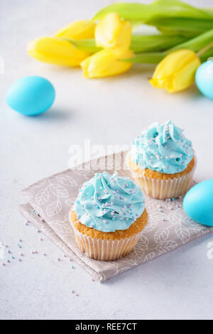 Vanilla cupcakes avec glaçage bleu et les oeufs colorés pour Pâques. Banque D'Images