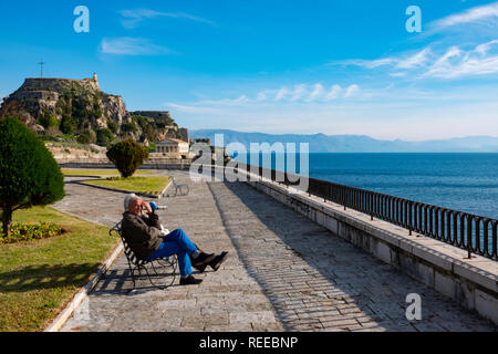 La ville de Corfou Corfou Grèce un couple de personnes âgées se trouve le long de la mer près de l'ancienne forteresse de prendre au soleil Banque D'Images