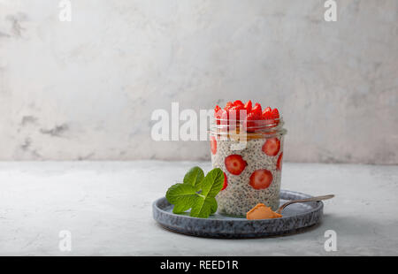 Petit-déjeuner sain. nuit du gruau avec des fraises, chia graines dans un bocal de verre sur fond gris Banque D'Images