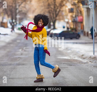 Cheerful jeune femme noire en écharpe et chandail est à pied de la rue et de sourire. Banque D'Images