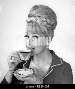 Café dans les années 1960. Une femme est de boire du café à partir d'un 1960 coffeecup avec un motif à rayures. Elle a ses cheveux dans la ruche typique hairstyle, dont les cheveux longs s'entasse sur le dessus de la tête et de donner une certaine ressemblance avec la forme d'une ruche traditionnelle. Suède 1962 Banque D'Images