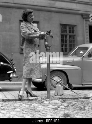 À la mode dans les années 1950. Une jeune femme porte un manteau de la mode d'automne 1950. Elle paie pour son ticket de parking dans le parcomètre dans une rue. La Suède des années 1950. Kristoffersson Photo réf 321a-5 Banque D'Images