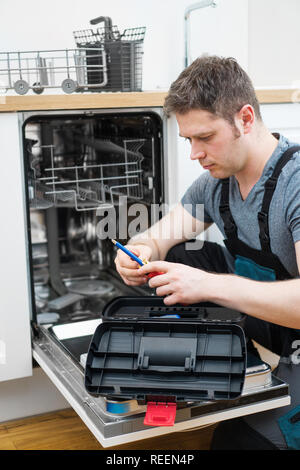 Bricoleur professionnel dans des combinaisons réparation lave-vaisselle domestiques dans la cuisine. Banque D'Images