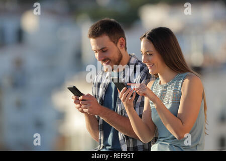 Couple heureux en utilisant leur téléphone intelligent à l'extérieur dans une ville au coucher du soleil Banque D'Images