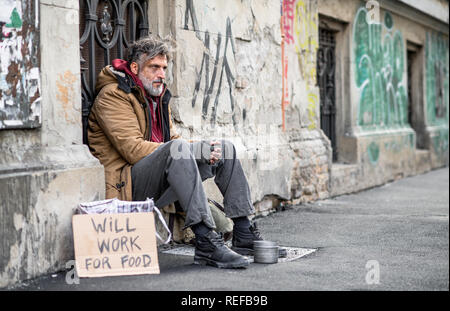 Les sans-abri mendiant homme assis à l'extérieur en ville pour demander de l'argent don. Banque D'Images