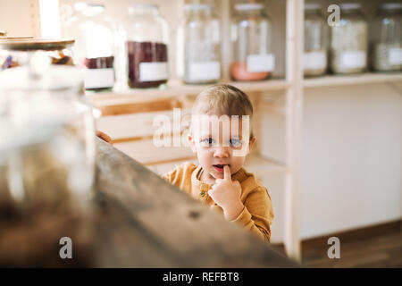 Un petit bébé garçon debout au comptoir dans zéro déchets shop. Banque D'Images