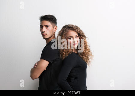 Portrait d'un jeune couple debout dos à dos dans un studio, portant des vêtements noirs. Banque D'Images