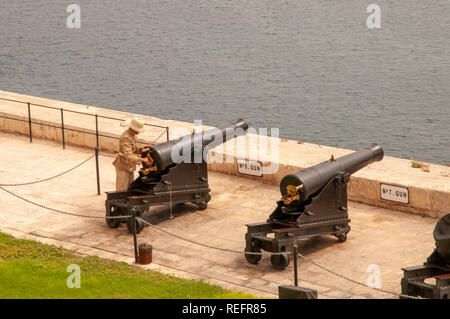 Vieux soldat charger deux canons en bronze pour le midi salut en rendant hommage à la batterie, Jardins Barrakka supérieur de La Valette, Malte. Banque D'Images