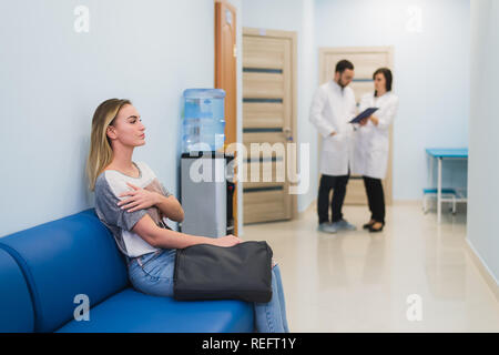 Femme attendant à un couloir de l'hôpital pour un contrôle des résultats. Se sentir nerveux. Médecins qui parlent sur un arrière-plan. Banque D'Images
