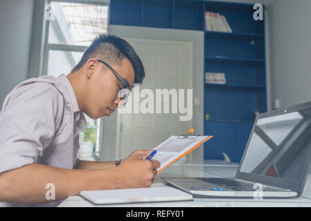 Vue latérale du Young Asian man écrit remarque dans l'ordinateur portable Banque D'Images