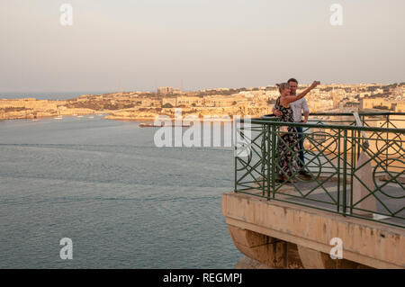 Un couple de prendre un en haut selfies Jardins Barrakka à Valletta, Malte, avec le Grand Port et Kalkara en arrière-plan. Banque D'Images