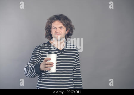 Portrait of happy bel homme aux cheveux noirs bouclés en pullover rayé avec du papier tasse de café du matin isolé sur fond gris. Bon matin avec te Banque D'Images