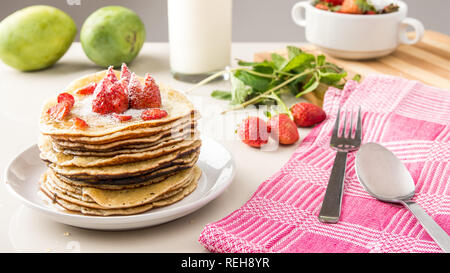 Pile de crêpes sur la table avec des fraises, menthe, miel et sucre. Banque D'Images