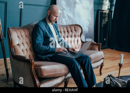 Joli succès adultes surpris homme chauve avec barbe en fonction de travailler à l'ordinateur portable sur son cabinet riche Banque D'Images