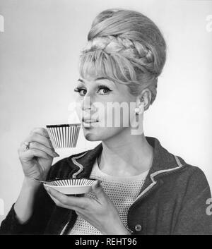 Café dans les années 1960. Une femme est de boire du café à partir d'un 1960 coffeecup avec un motif à rayures. Elle a ses cheveux dans la ruche typique hairstyle, dont les cheveux longs s'entasse sur le dessus de la tête et de donner une certaine ressemblance avec la forme d'une ruche traditionnelle. Suède 1962 Banque D'Images